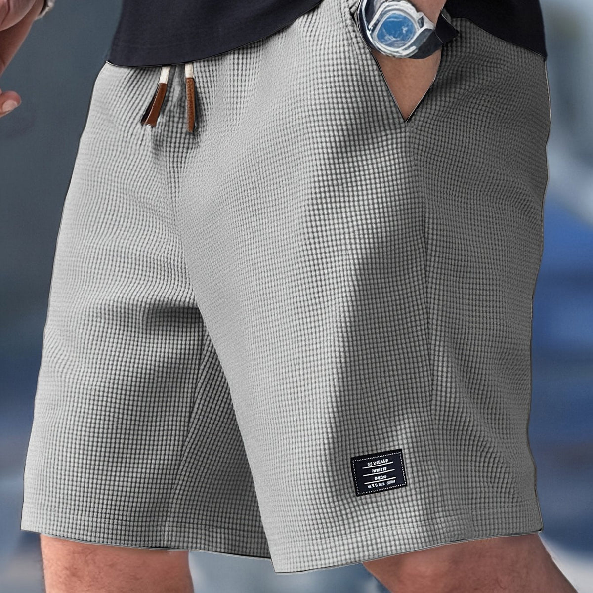 Light grey waffle-textured drawstring shorts worn by a model, one hand in the pocket, small woven label on the leg. 5