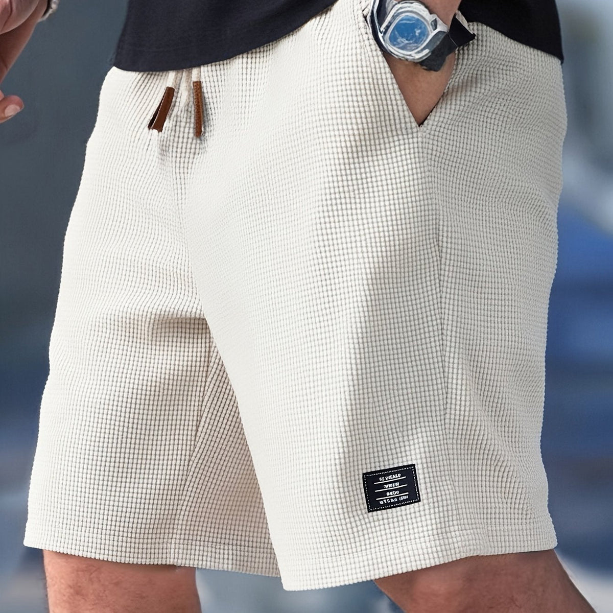 Cream waffle-textured drawstring shorts worn by a model with one hand in a pocket, a small woven label near the hem. 1