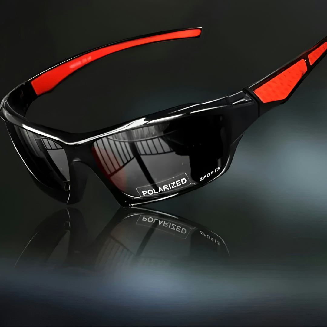 Black wraparound sports sunglasses with dark lenses and red arm inserts, angled view on a dark reflective surface 1
