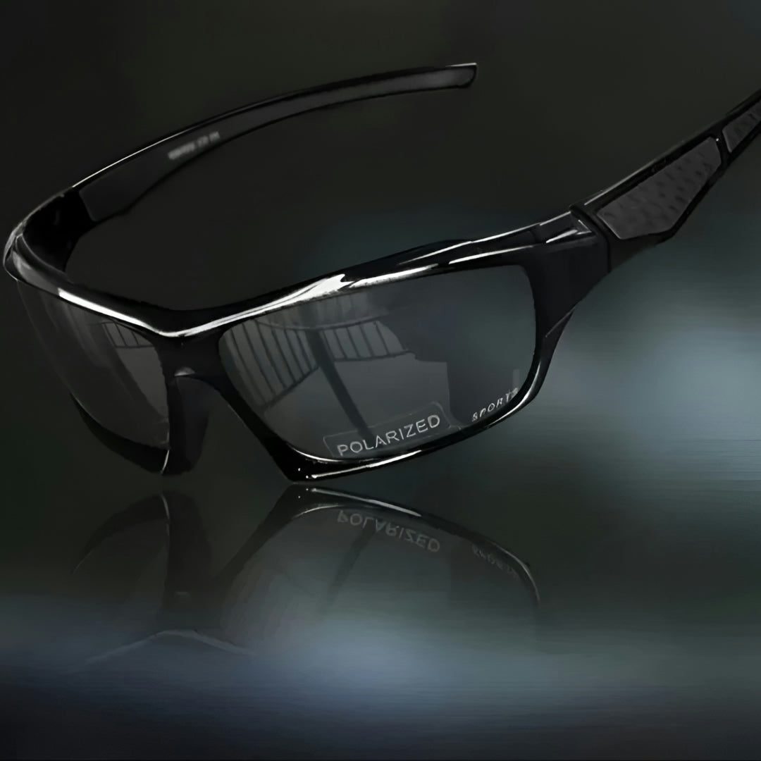 All-black sunglasses with dark grey lenses and black patterned arm inserts, angled view on a dark reflective surface 10