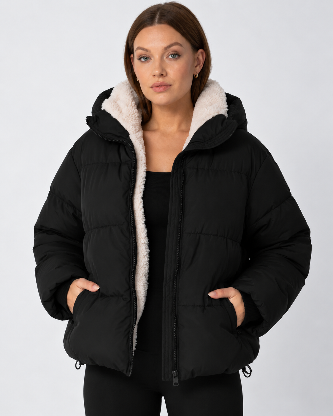 Front view of a model in a black puffer jacket worn open, with a cream fleece lining and hands in the pockets 11