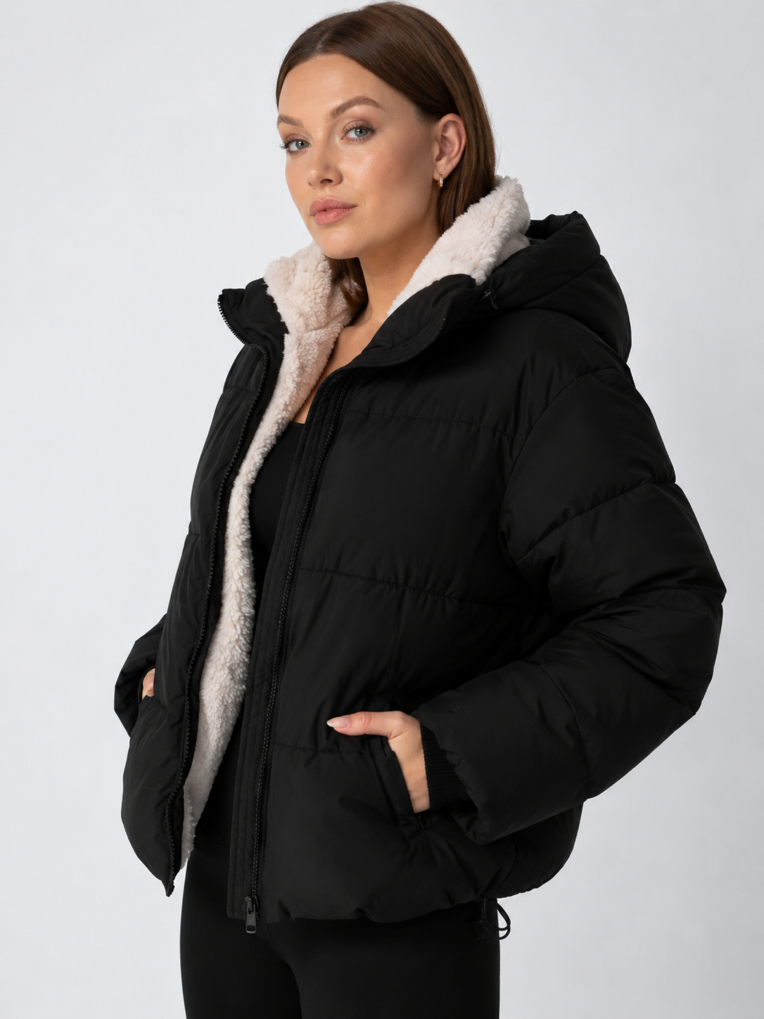 Angled view of a black puffer jacket with the hood up, showing the cream fleece lining and zipped pocket 12