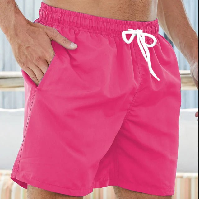 Pink swim trunks with a white drawstring, worn by a model with one hand resting in a side pocket. 3