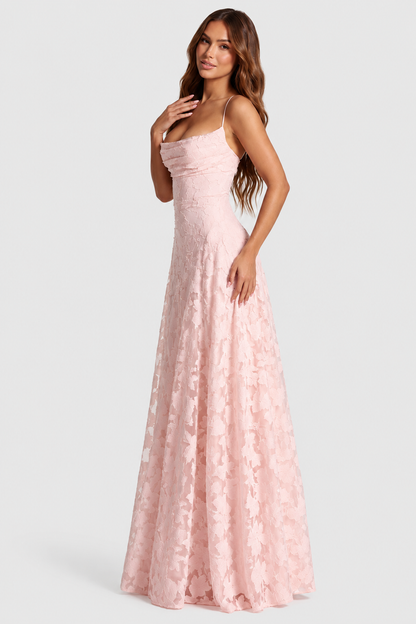 Model in pale pink floral lace gown turned three-quarters to the camera, one hand on her chest, showing the draped cowl neckline. 1