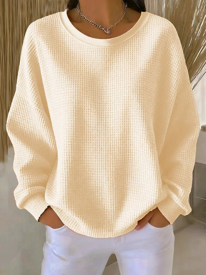 Model wearing the waffle-knit jumper in pale cream, with relaxed drop shoulders and ribbed cuffs, paired with white trousers. 4