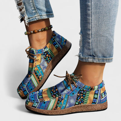 Model wearing blue, teal and mustard geometric-print lace-up shoes with a cork-effect sole, paired with ripped jeans and a beaded anklet. 6