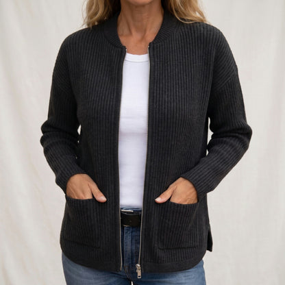 Woman wearing the charcoal ribbed knit cardigan unzipped over a white top and jeans, hands resting in the deep front pockets. 2
