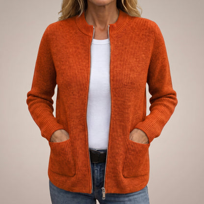 Woman wearing the burnt orange ribbed knit cardigan unzipped over a white top and jeans, hands tucked into the front pockets. 4