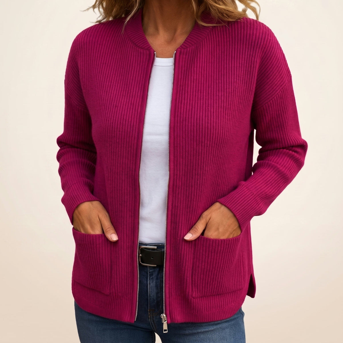 Woman wearing the magenta ribbed zip-up cardigan open over a white top and jeans, hands resting in the front pockets. 5