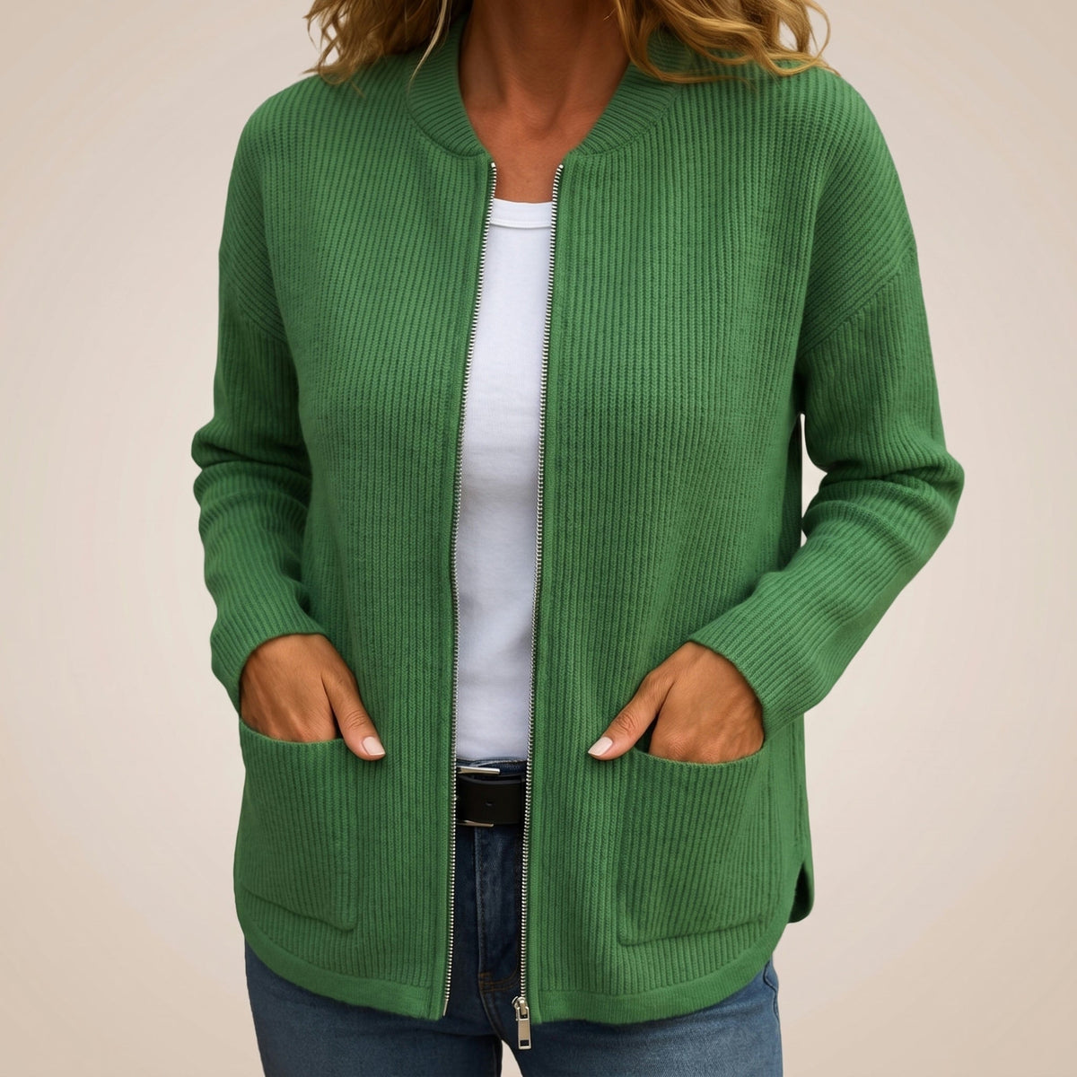 Woman wearing the green ribbed-knit cardigan unzipped over a white top and jeans, hands resting in the deep front pockets. 6