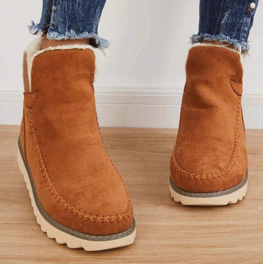 Front view of tan suede-look ankle boots with decorative stitching and a soft fleece-lined opening, worn with frayed jeans. 5