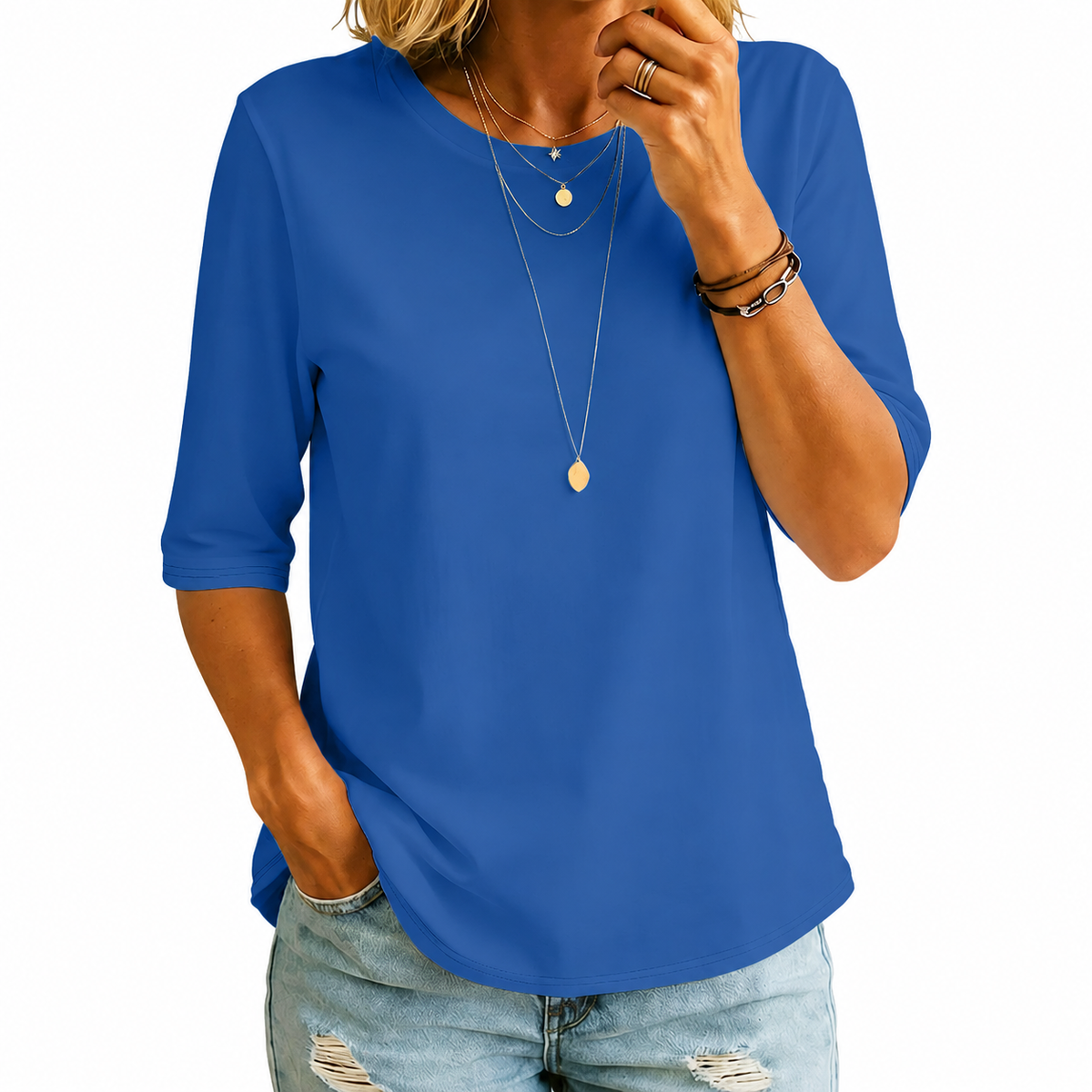 Woman wearing the round-neck half-sleeve t-shirt in vivid royal blue, with layered gold necklaces and ripped jeans, against a plain white background. 6