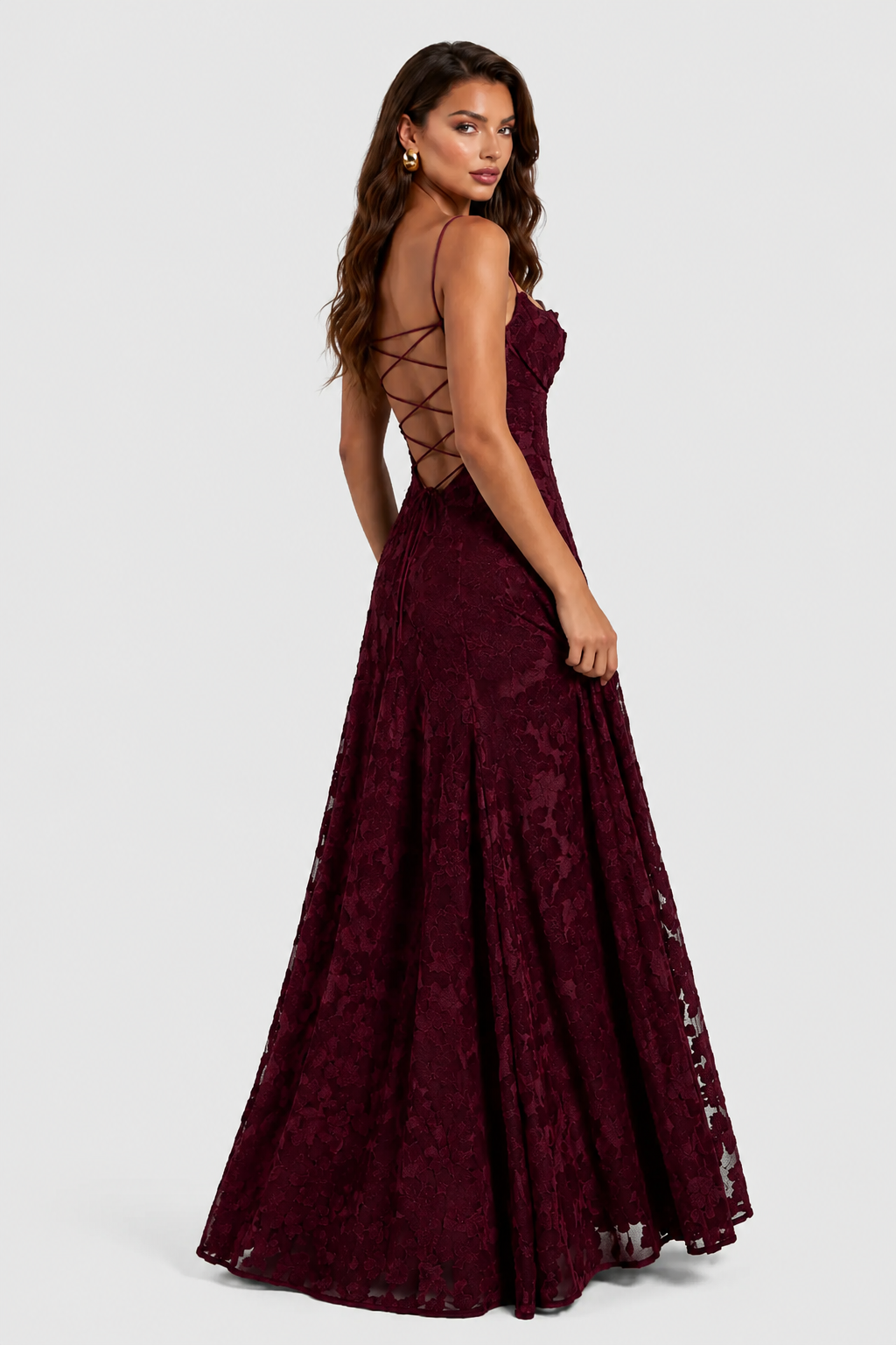 Back view of a burgundy lace gown on a model glancing over her shoulder, showing criss-cross lace-up open back. 3
