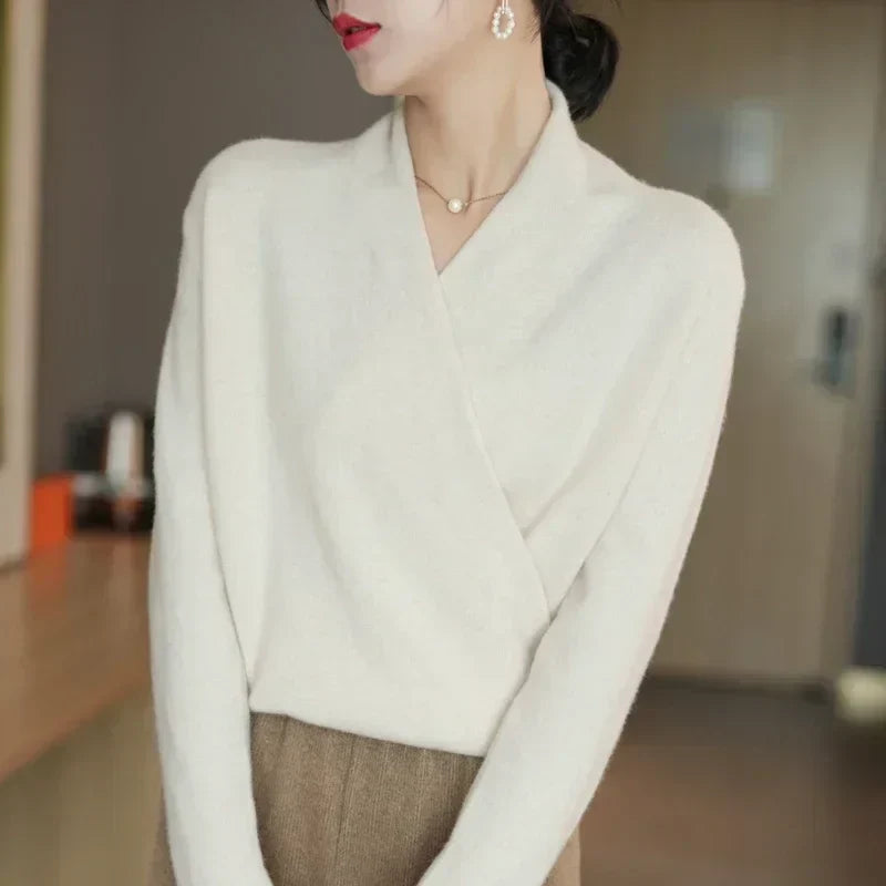 Model standing sideways in cream wrap jumper, pearl earring and necklace, with brown trousers 16