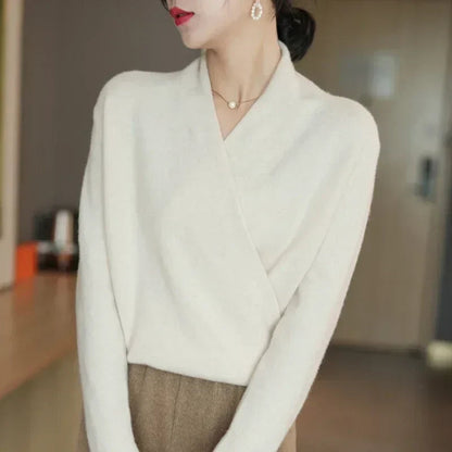Model standing sideways in cream wrap jumper, pearl earring and necklace, with brown trousers 16