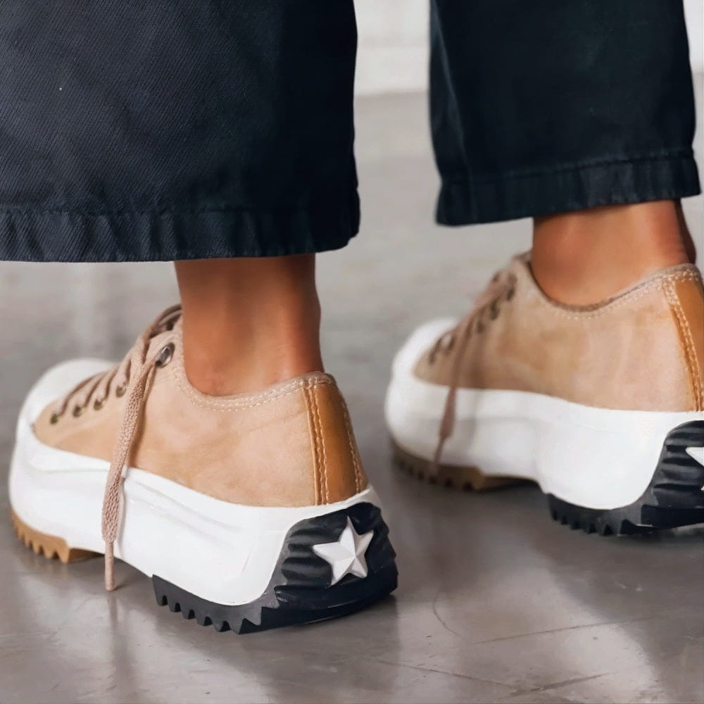 Rear view of beige platform trainers worn with black trousers, showing the heel panel and the star detail on the black heel tread. 2