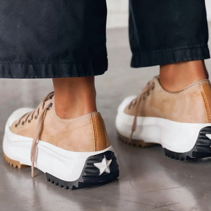 Rear view of beige platform trainers worn with black trousers, showing the heel panel and the star detail on the black heel tread. 2