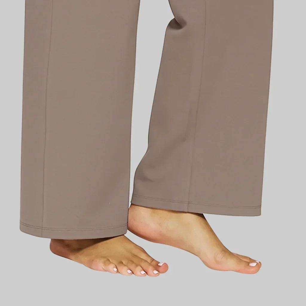 Close-up of the wide, straight hems of the taupe trousers, with stitched hem edges and a model's bare feet. 5