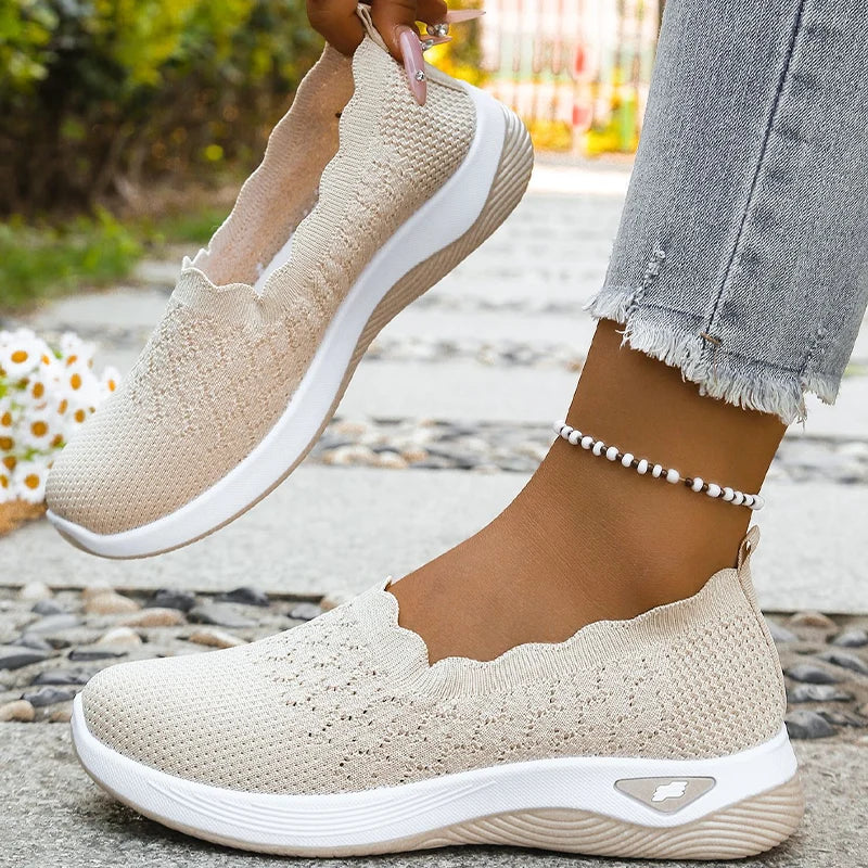 Beige slip-on shoe held up in one hand while the other foot wears its pair, showing the interior 9