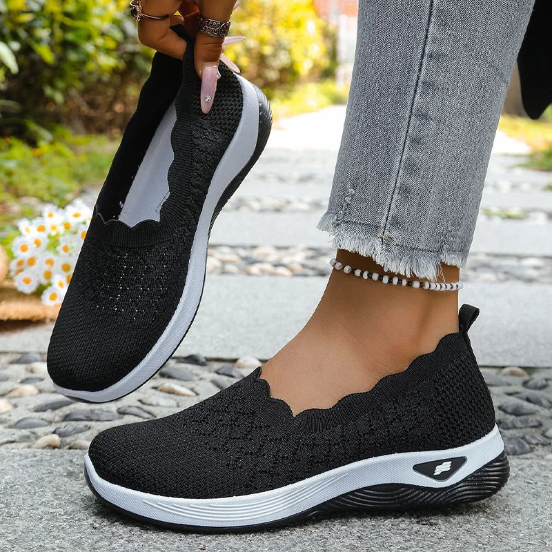 Black knit slip-on shoes with white midsole, one lifted to show the inside, the other worn 13