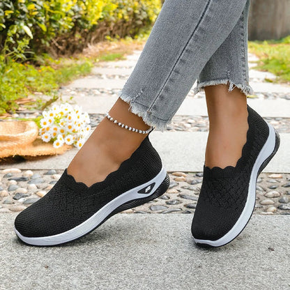 Black knit slip-on shoes with scalloped collar worn mid-step on a paved path 14