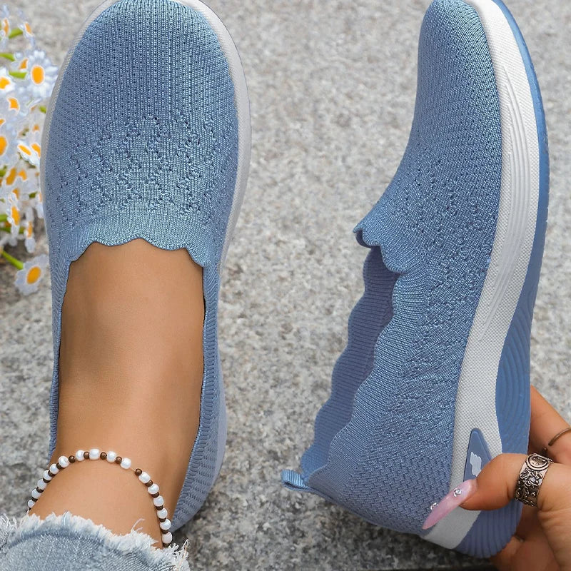 Top-down view of blue knit slip-on shoes with scalloped collar, one worn and one held 16