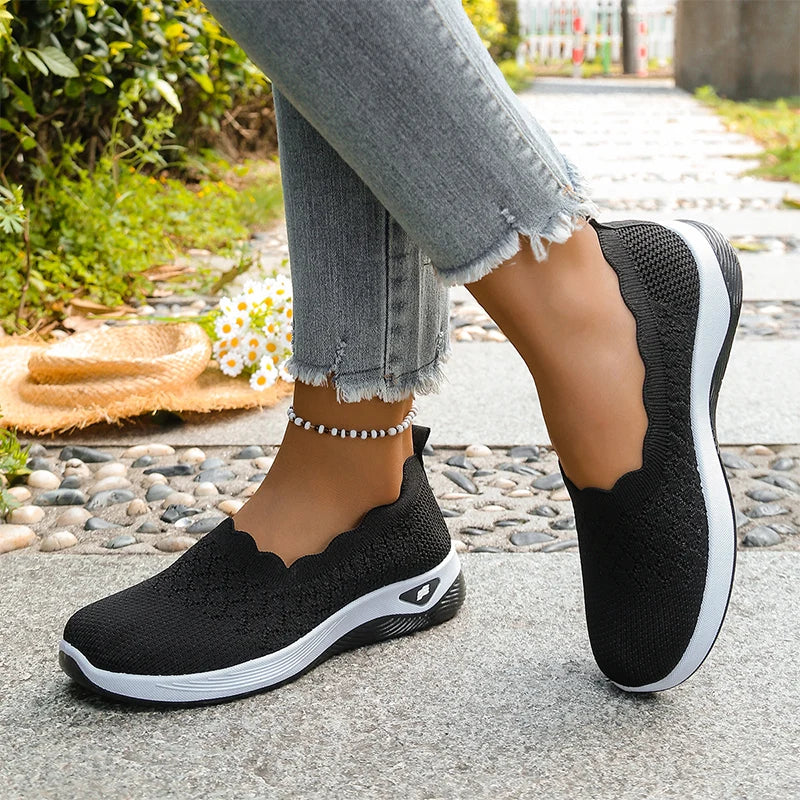 Black knit slip-on shoes worn with frayed grey jeans and a beaded anklet, angled side view 15