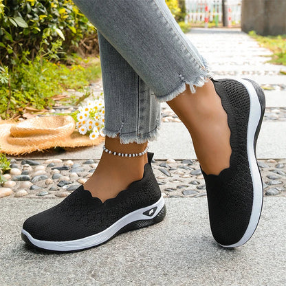 Black knit slip-on shoes worn with frayed grey jeans and a beaded anklet, angled side view 15
