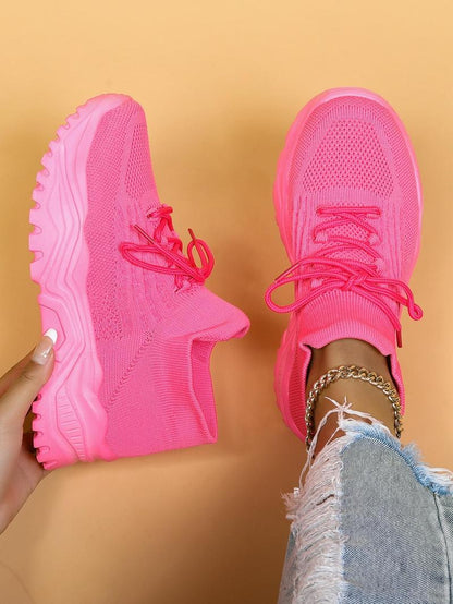 Top-down view of bright pink knit sneakers with chunky pink soles, one held in a hand and one worn with distressed jeans. 14