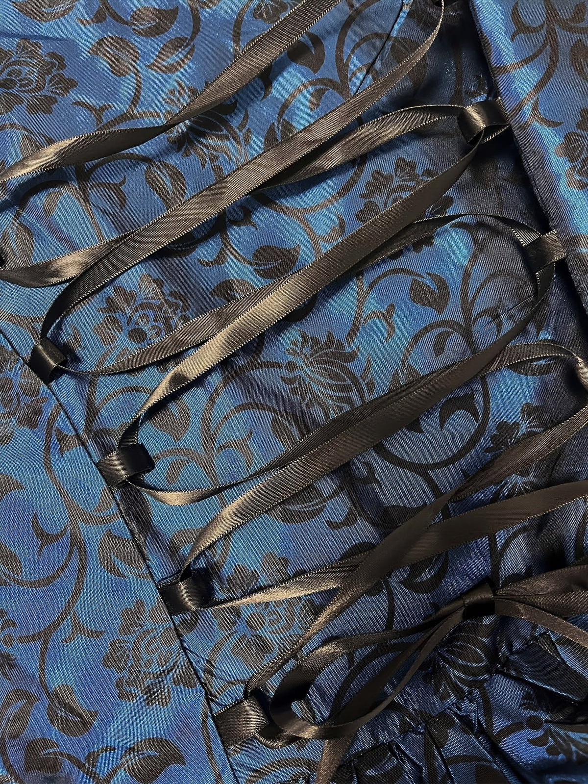Close-up of the black satin ribbon lacing across the navy floral brocade fabric at the back of the dress. 5