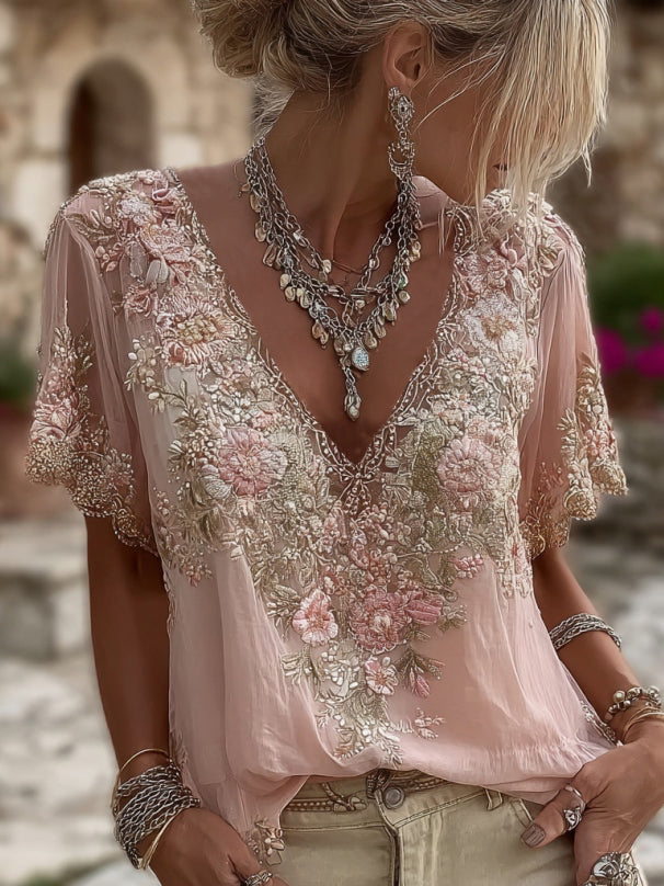 Model in a pale pink blouse with floral embroidery, layered silver necklaces and cream trousers, tall crop 1