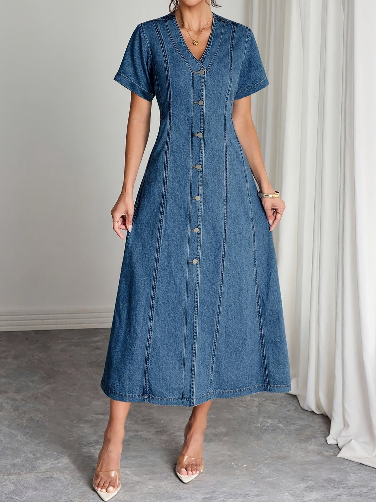 Front view of the V-neck denim midi dress on a model, arms relaxed, with clear heels 3