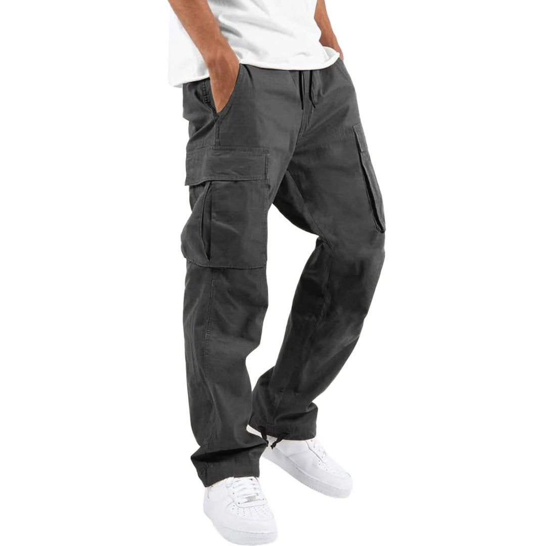 Model wearing dark grey cargo trousers with drawstring waist and large side flap pockets, paired with a white t-shirt and trainers. 8