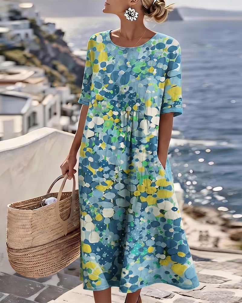 Model wearing the dress in a blue, yellow and green pebble-style floral print by the sea 9