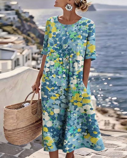 Model wearing the dress in a blue, yellow and green pebble-style floral print by the sea 9