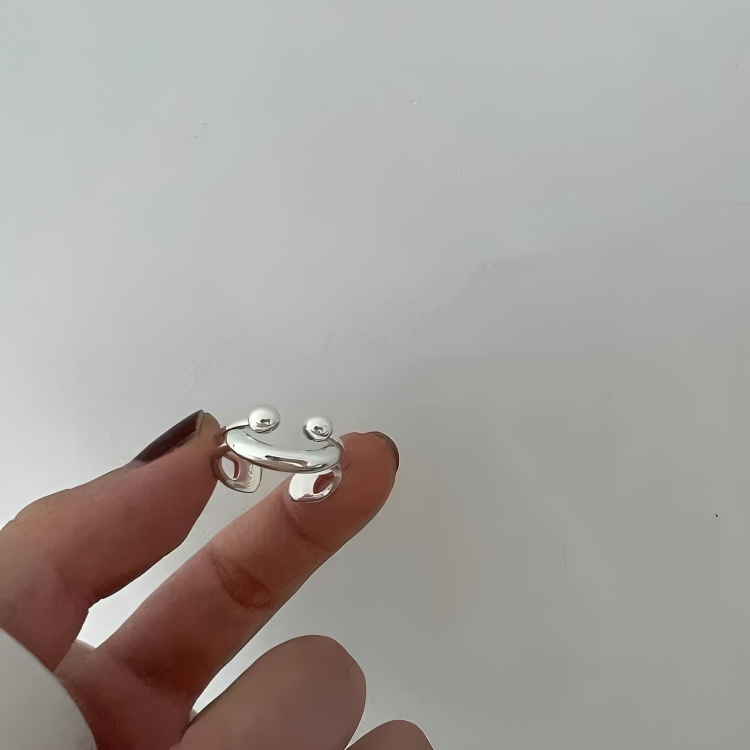 Silver smile ring held between two fingertips against a plain pale background, showing the open band and cut-out shapes at the back. 4