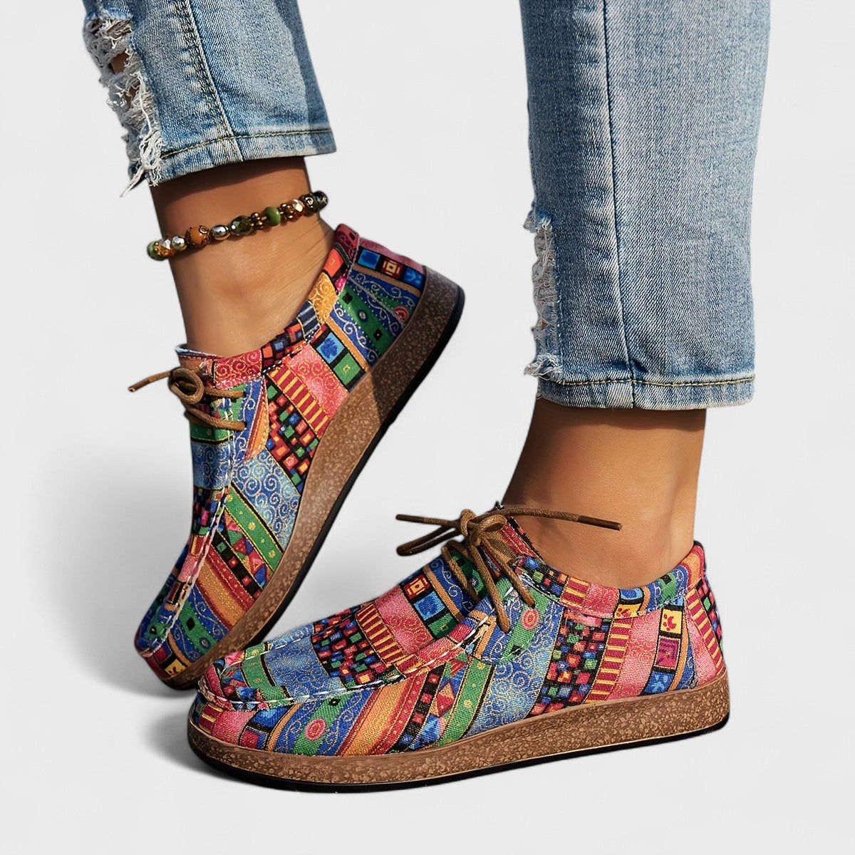 Side view of a model wearing multicoloured striped lace-up shoes in blue, green and pink with a cork-style sole and beaded anklet. 3