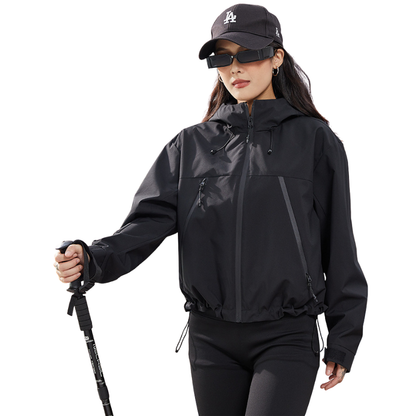 Black jacket worn by a model holding a trekking pole, with the hood drawcords and gathered hem visible. 14