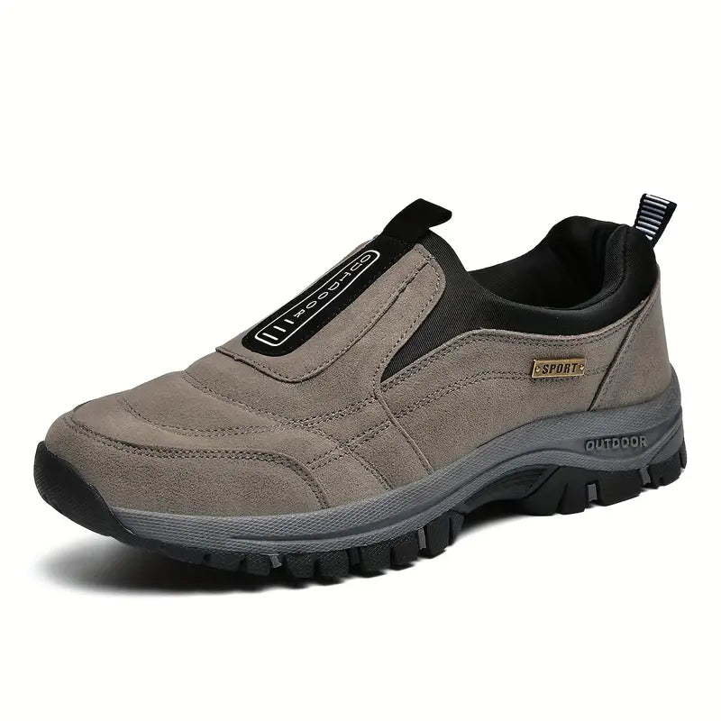 Grey-brown suede-look slip-on shoe seen from the front three-quarter angle, with black elastic side panel and thick chunky grey and black tread sole. 1