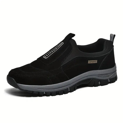 Black suede-look slip-on shoe seen from the front three-quarter angle, with elastic side panel, rear pull loop and chunky grey tread sole. 3