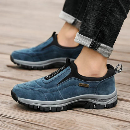 Blue slip-on shoes worn by a model in rolled-up dark jeans on a wooden boardwalk, showing side profile and grey tread sole. 5