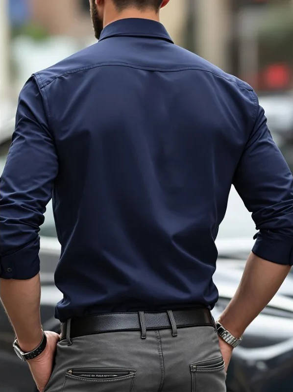 Back view of a model in the navy shirt with sleeves rolled, grey trousers and a black belt 10