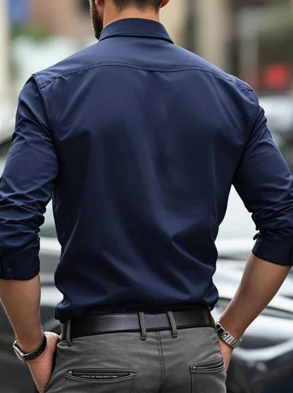 Back view of a model in the navy shirt with sleeves rolled, grey trousers and a black belt 10