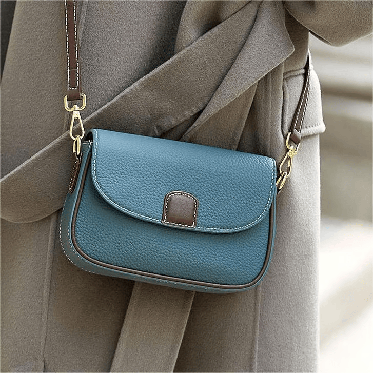 Teal blue leather crossbody bag with brown trim, worn over a grey wool coat 4