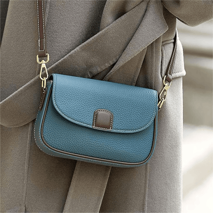 Teal blue leather crossbody bag with brown trim, worn over a grey wool coat 4