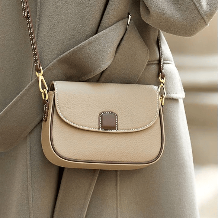 Pale taupe leather crossbody bag with brown flap tab, worn over a grey-green wool coat 3