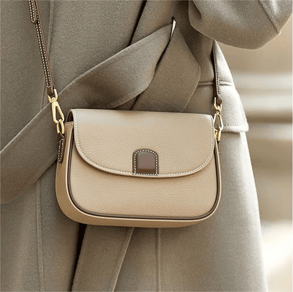 Pale taupe leather crossbody bag with brown flap tab, worn over a grey-green wool coat 3