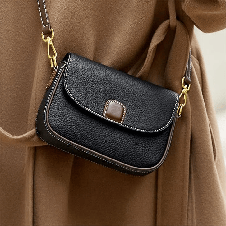 Black pebbled leather saddle bag with brown tab, worn crossbody over a camel wool coat 1