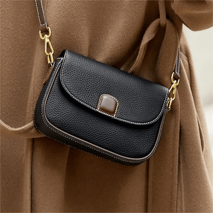 Black pebbled leather saddle bag with brown tab, worn crossbody over a camel wool coat 1