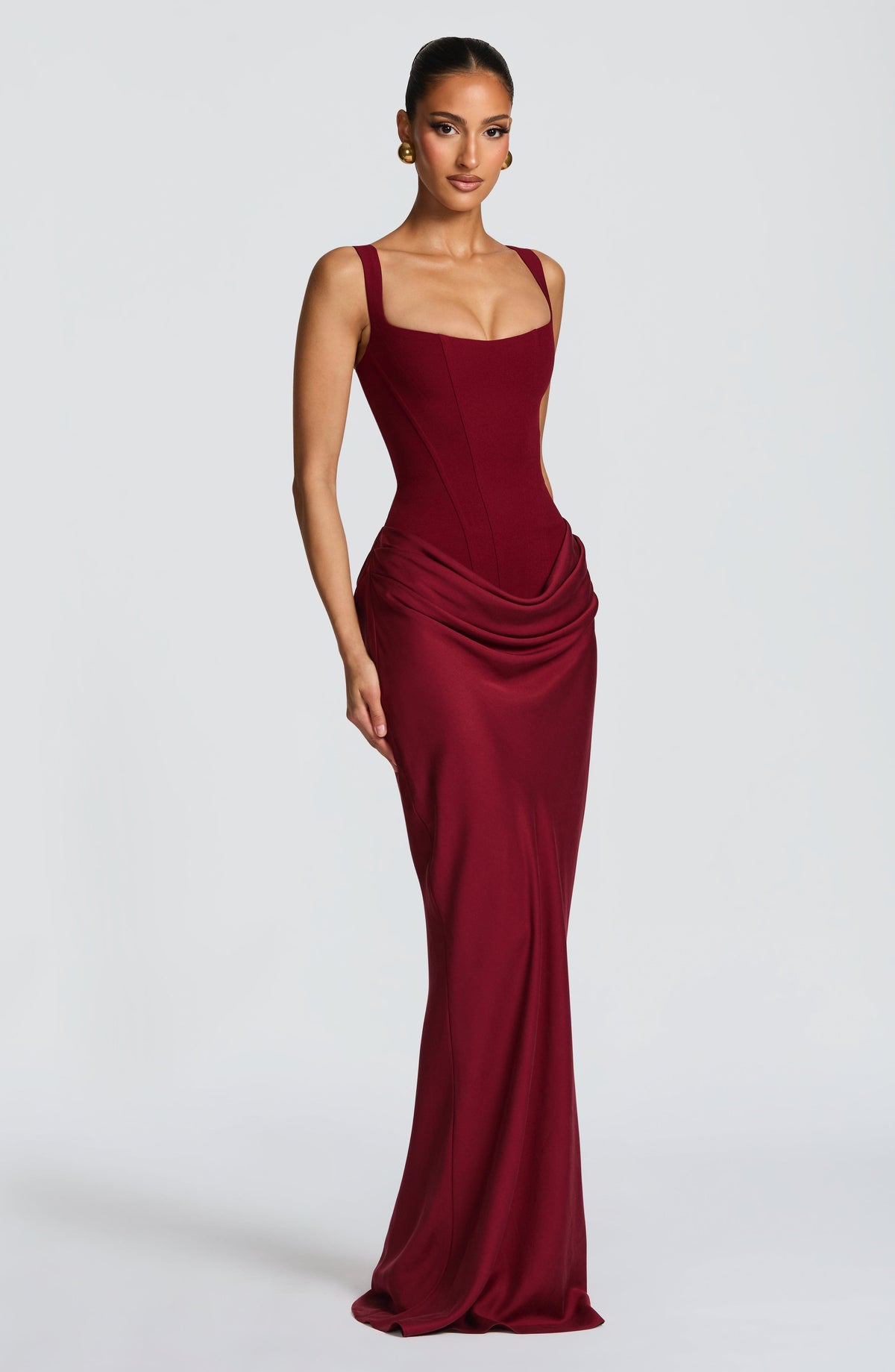 Three-quarter front view of the burgundy maxi dress on a model, showing the corset seams, draped hip and floor-length skirt. 24